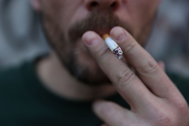 Photo of Man smoking cigarette on blurred background, closeup