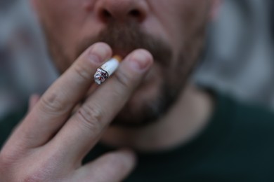 Photo of Man smoking cigarette on blurred background, closeup