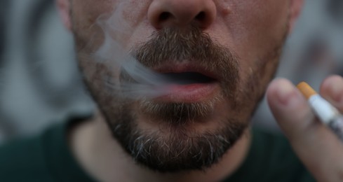 Photo of Man smoking cigarette on blurred background, closeup