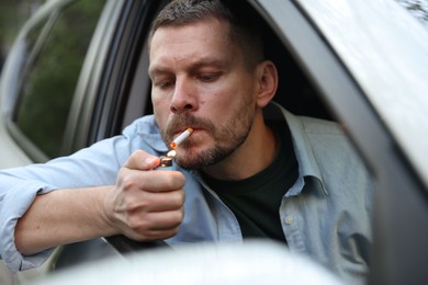 Photo of Man lighting cigarette in car, view from outside
