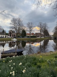 Photo of Leiden, Netherlands - March 22, 2025: Beautiful buildings and trees near city canal with moored boats on cloudy day