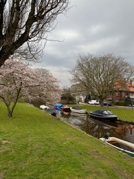 Photo of Leiden, Netherlands - March 22, 2025: Beautiful buildings and trees near city canal with moored boats on cloudy day