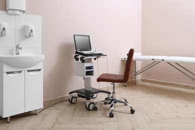 Photo of Modern ultrasound machine, chair and examination bed in clinic