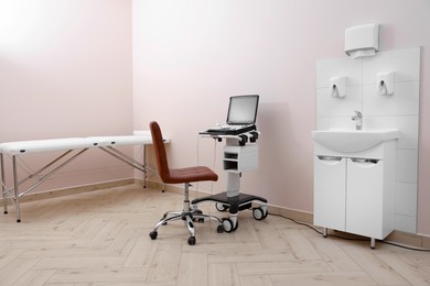 Photo of Modern ultrasound machine, chair and examination bed in clinic