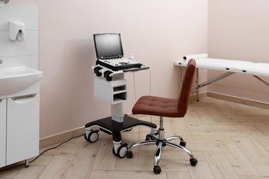 Photo of Modern ultrasound machine, chair and examination bed in clinic