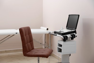Photo of Modern ultrasound machine, chair and examination bed in clinic