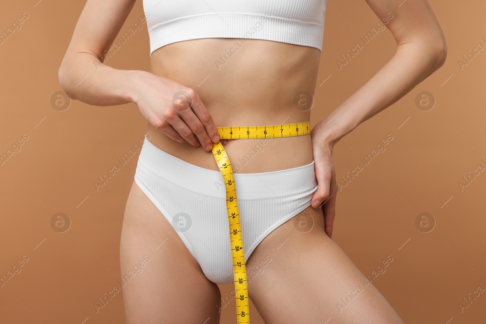 Woman with slim body and measuring tape on beige background, closeup Photo of Woman with slim body and measuring tape on beige background, closeup