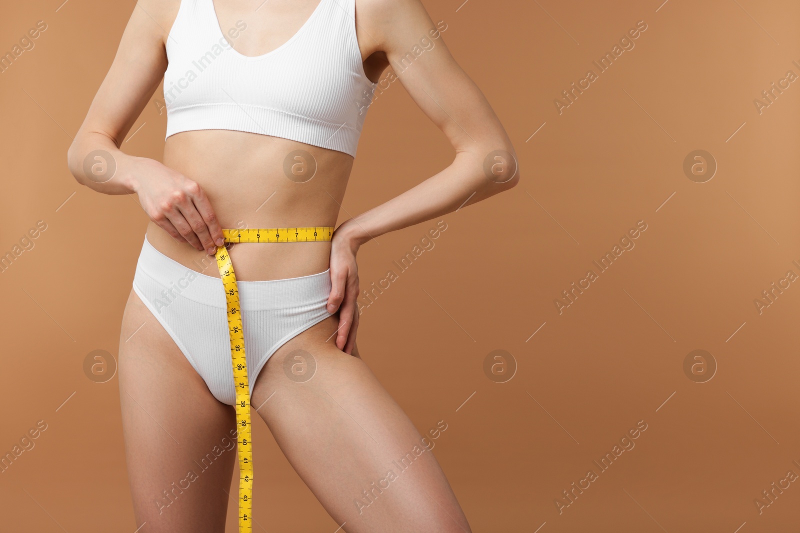 Woman with slim body and measuring tape on beige background, closeup. Space for text Photo of Woman with slim body and measuring tape on beige background, closeup. Space for text