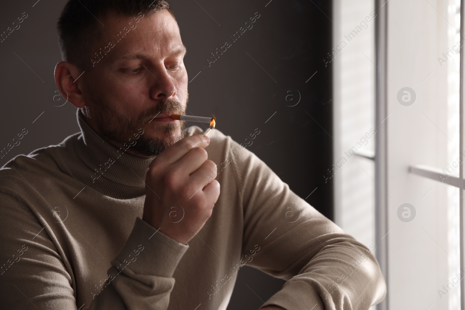 Man lighting cigarette with match near window indoors Photo of Man lighting cigarette with match near window indoors