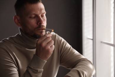 Photo of Man lighting cigarette with match near window indoors