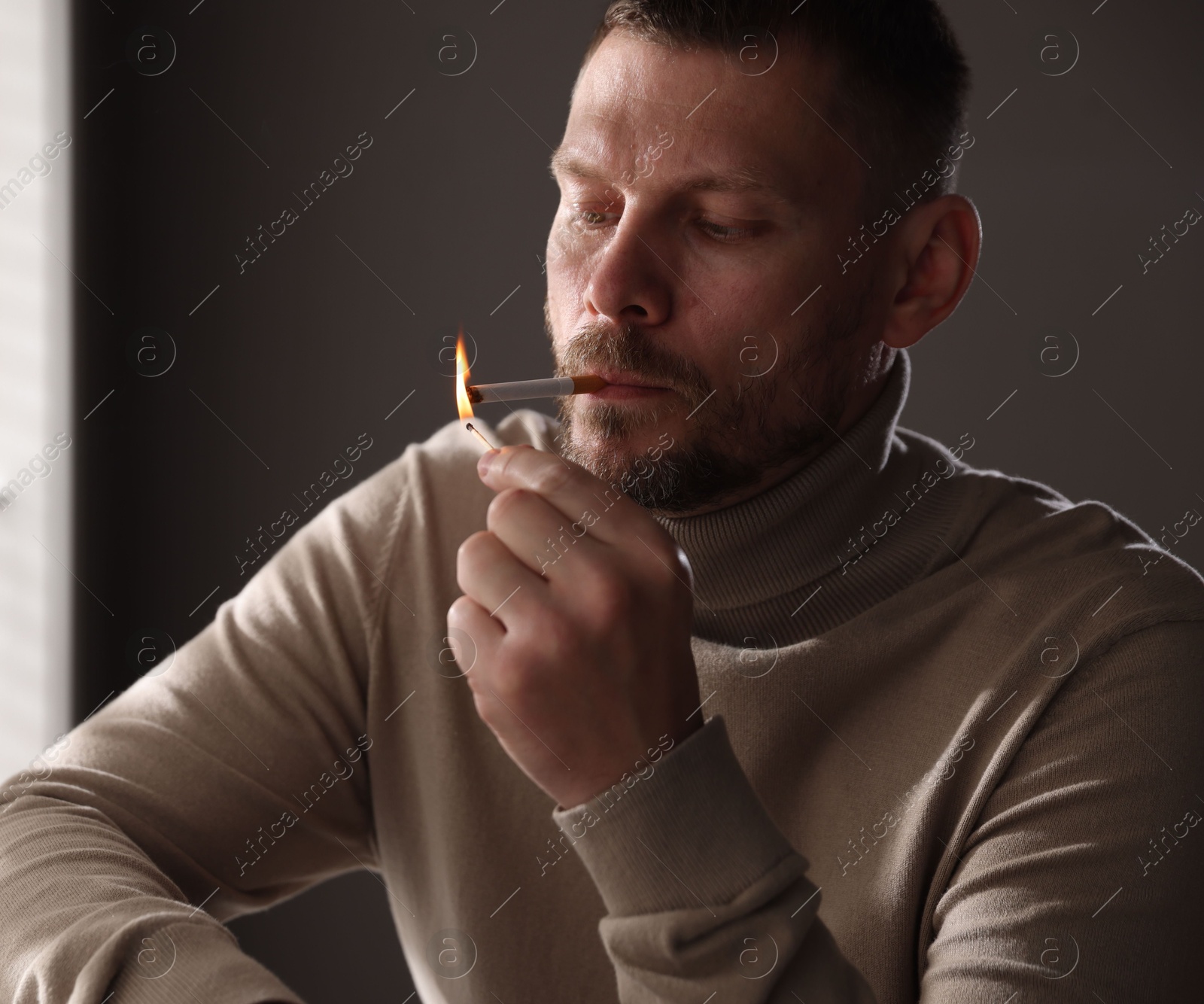 Man lighting cigarette with match near window indoors Photo of Man lighting cigarette with match near window indoors