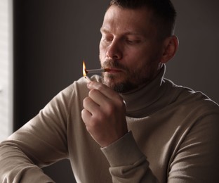 Photo of Man lighting cigarette with match near window indoors
