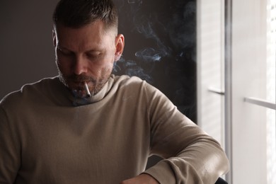 Photo of Man smoking cigarette near window in room