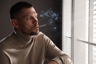 Photo of Man smoking cigarette near window in room