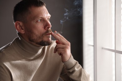 Photo of Man smoking cigarette near window in room