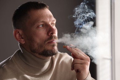 Photo of Man smoking cigarette near window in room