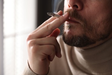 Photo of Man smoking cigarette on blurred background, closeup
