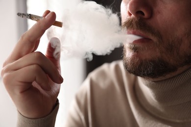 Photo of Man smoking cigarette on blurred background, closeup
