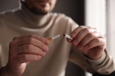 Photo of Man holding broken cigarette on blurred background, closeup. Stop smoking