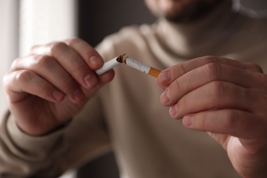 Photo of Man holding broken cigarette on blurred background, closeup. Stop smoking