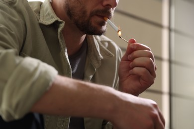 Photo of Man lighting cigarette with match on blurred background, closeup