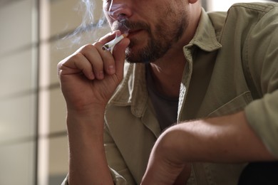 Photo of Man smoking cigarette on blurred background, closeup