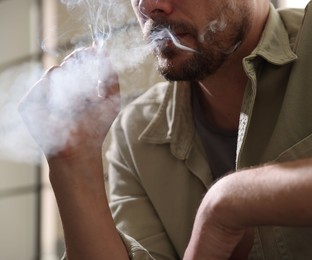 Photo of Man smoking cigarette on blurred background, closeup