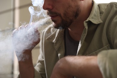 Photo of Man smoking cigarette on blurred background, closeup