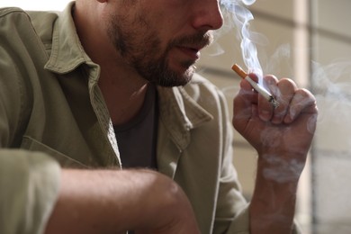 Photo of Man smoking cigarette on blurred background, closeup