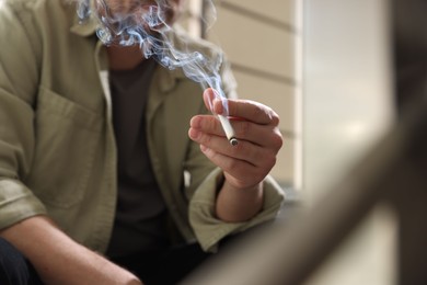 Photo of Man smoking cigarette on blurred background, closeup
