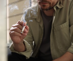 Photo of Man smoking cigarette on blurred background, closeup
