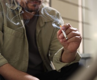 Photo of Man smoking cigarette on blurred background, closeup