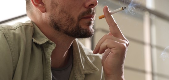 Photo of Man smoking cigarette on blurred background, closeup