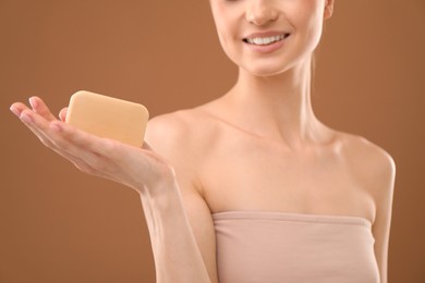 Photo of Smiling woman with soap bar on brown background, closeup