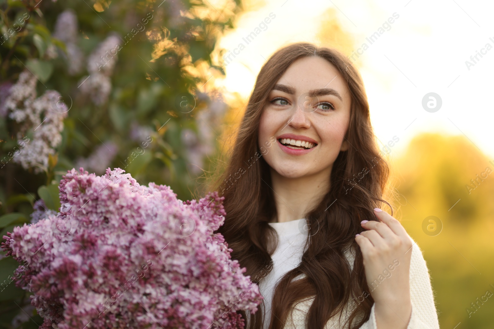 Portrait of smiling woman with lilac flowers outdoors in morning Photo of Portrait of smiling woman with lilac flowers outdoors in morning