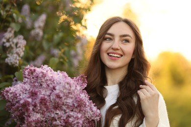 Photo of Portrait of smiling woman with lilac flowers outdoors in morning
