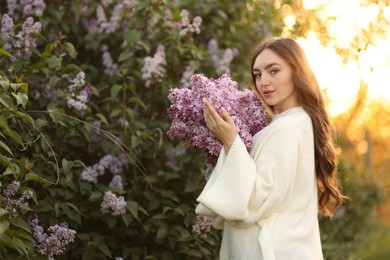 Photo of Beautiful woman with lilac flowers near bush outdoors in morning