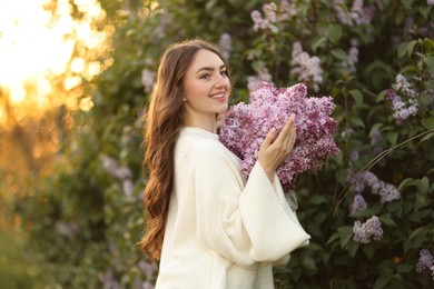 Photo of Smiling woman with bouquet of lilac flowers near bush outdoors in morning