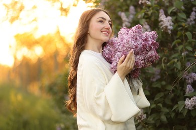 Photo of Smiling woman with bouquet of lilac flowers near bush outdoors in morning