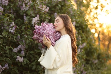 Photo of Beautiful woman with bouquet of lilac flowers near bush outdoors in morning