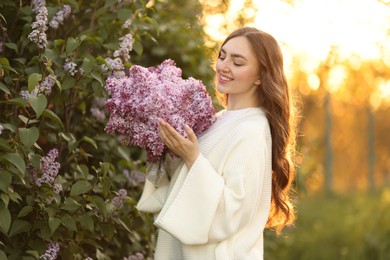 Photo of Smiling woman with bouquet of lilac flowers near bush outdoors in morning