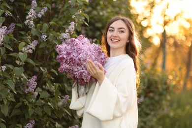 Photo of Smiling woman with bouquet of lilac flowers near bush outdoors in morning