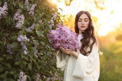 Photo of Beautiful woman with bouquet of lilac flowers near bush outdoors in morning