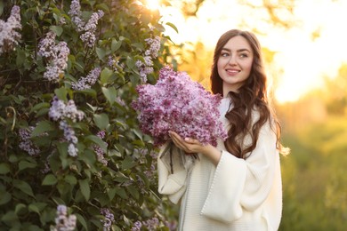 Photo of Smiling woman with bouquet of lilac flowers near bush outdoors in morning