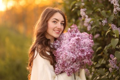 Photo of Smiling woman with bouquet of lilac flowers outdoors in morning