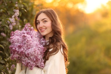 Photo of Smiling woman with bouquet of lilac flowers outdoors in morning. Space for text