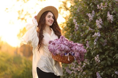 Photo of Smiling woman with basket of lilac flowers near bush outdoors in morning