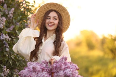 Photo of Smiling woman with basket of lilac flowers outdoors in morning. Space for text