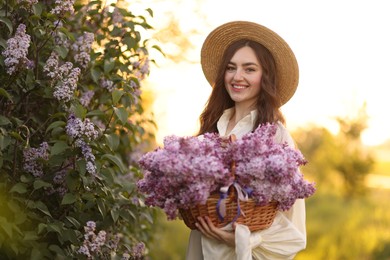 Photo of Smiling woman with basket of lilac flowers near bush outdoors in morning
