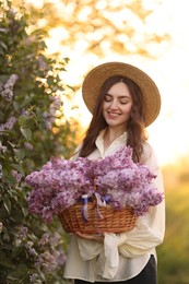 Photo of Smiling woman with basket of lilac flowers outdoors in morning